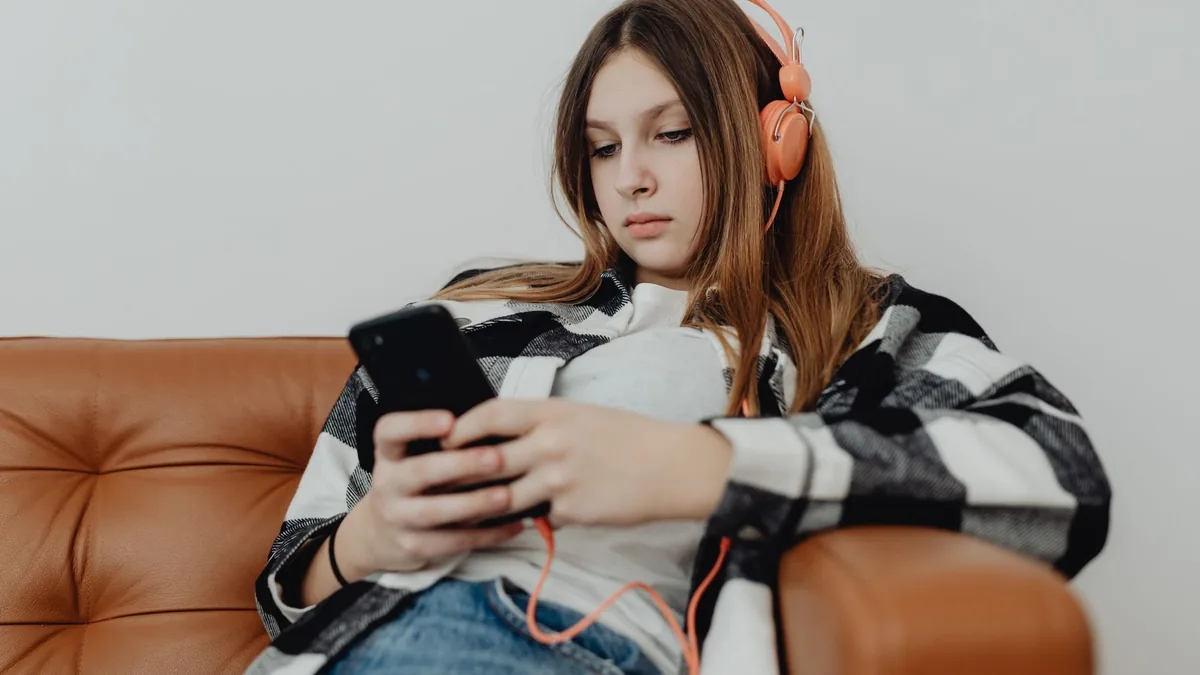 Девочка-подросток в наушниках со смартфоном на диване
